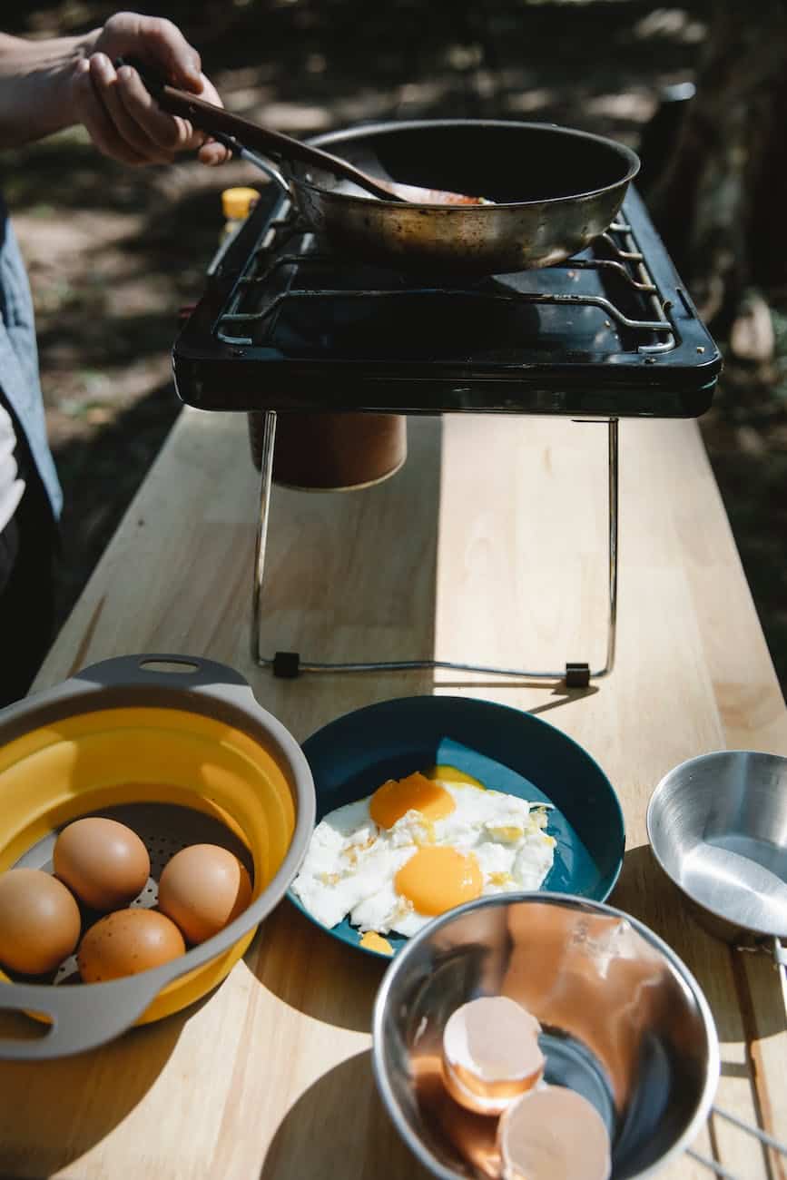 man frying eggs on stove in nature. Learn how to pack food for camping in Washington State.